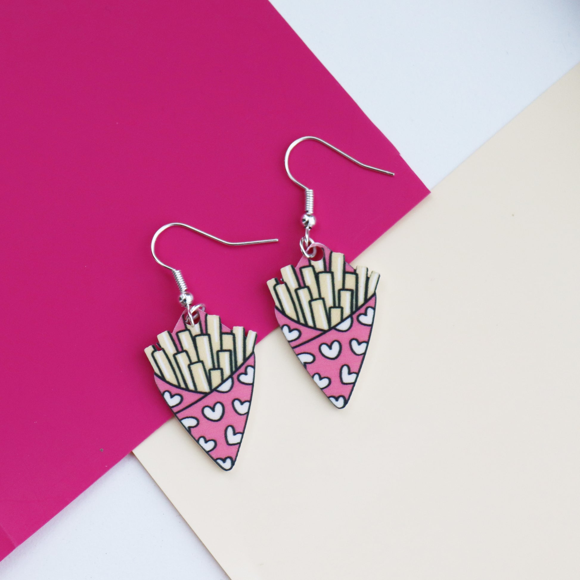 fries before guys earrings cut from acrylic and printed with a bag of chips design the bag of chips is pink and has hearts printed on it