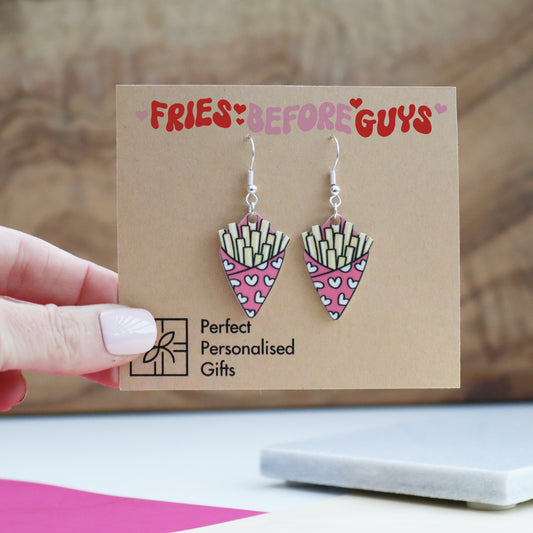 fries before guys earrings cut from acrylic and printed with a bag of chips design the bag of chips is pink shown on the backing card with the message fries before guys printed on the earring backing card