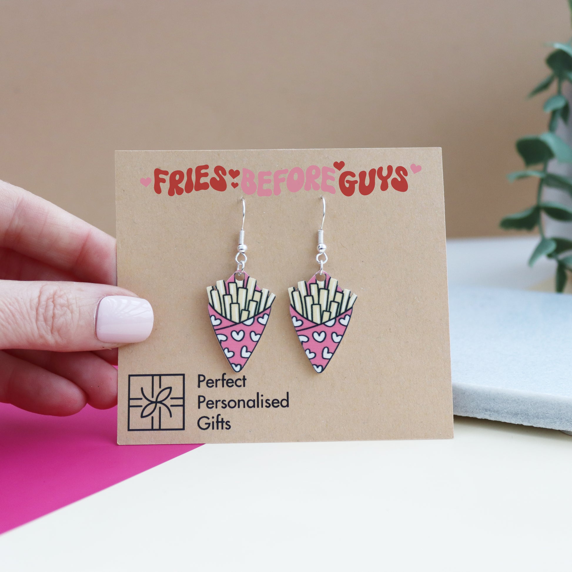 fries before guys earrings cut from acrylic and printed with a bag of chips design the bag of chips is pink shown on the backing card with the message fries before guys printed on the earring backing card