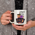 White mug reading 'Tarot and tea' with tarot cards, roses and an iced drink design, held in hands