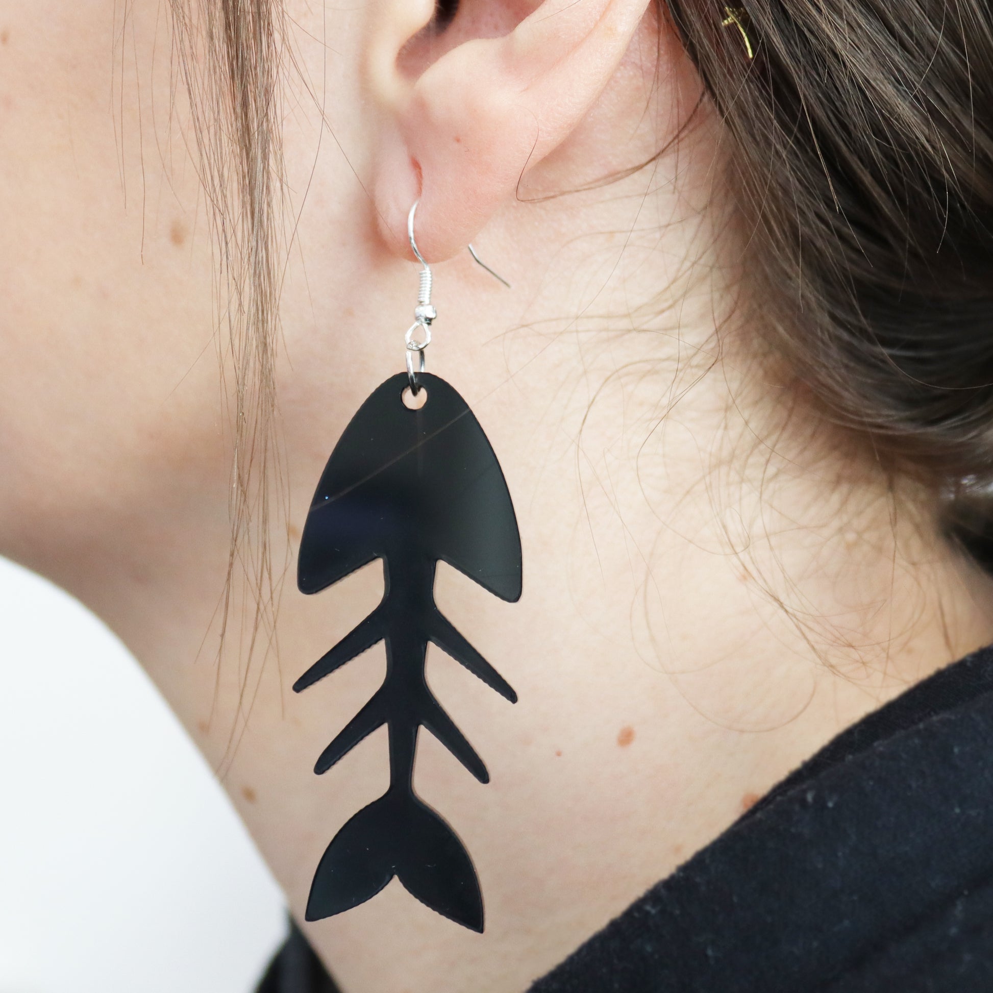 large fish bone earring cut from black acrylic and shown hanging in an ear