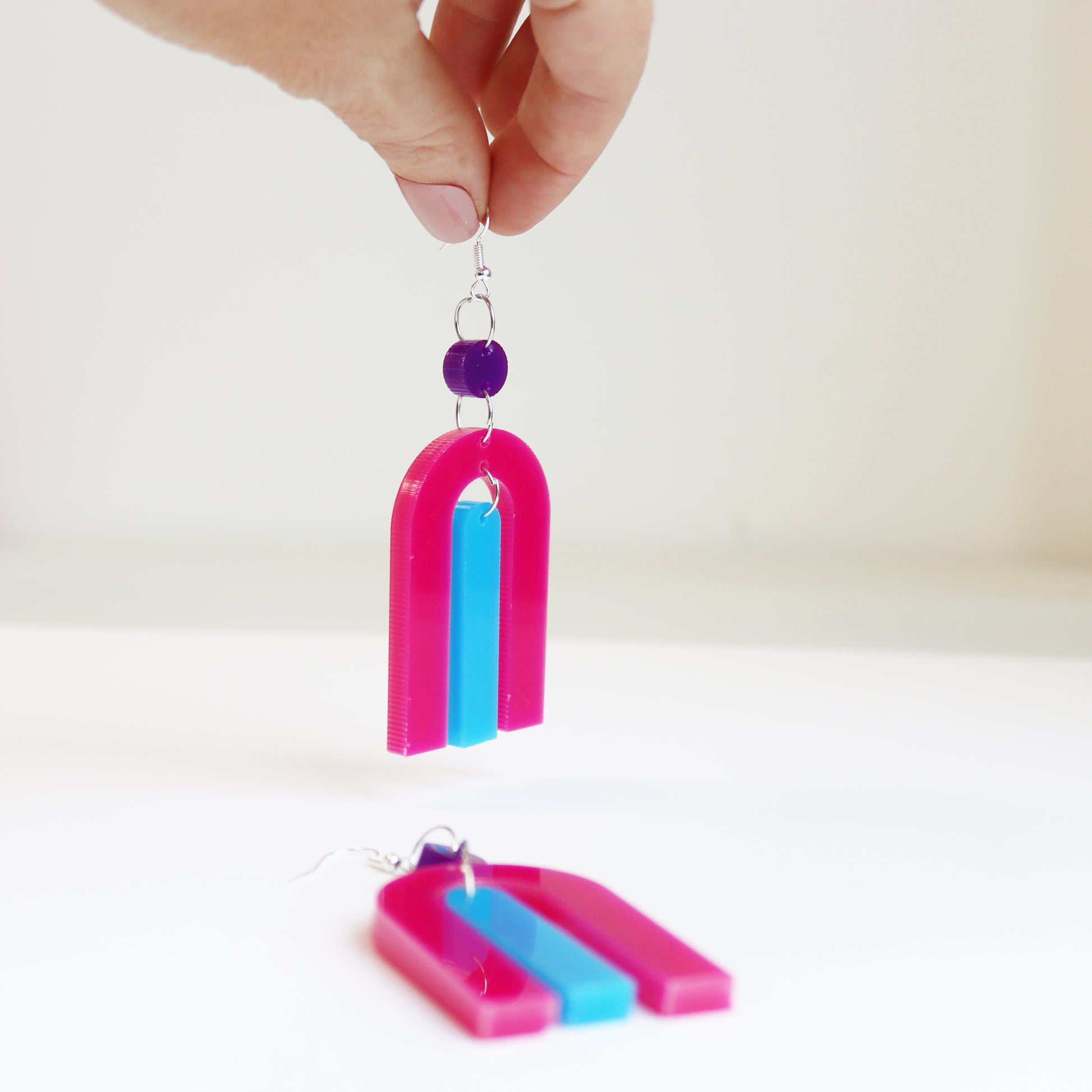 modern bright and colourful geometric arch dangle earrings cut from a purple, pink and turquoise acrylic shown on a mirrr background