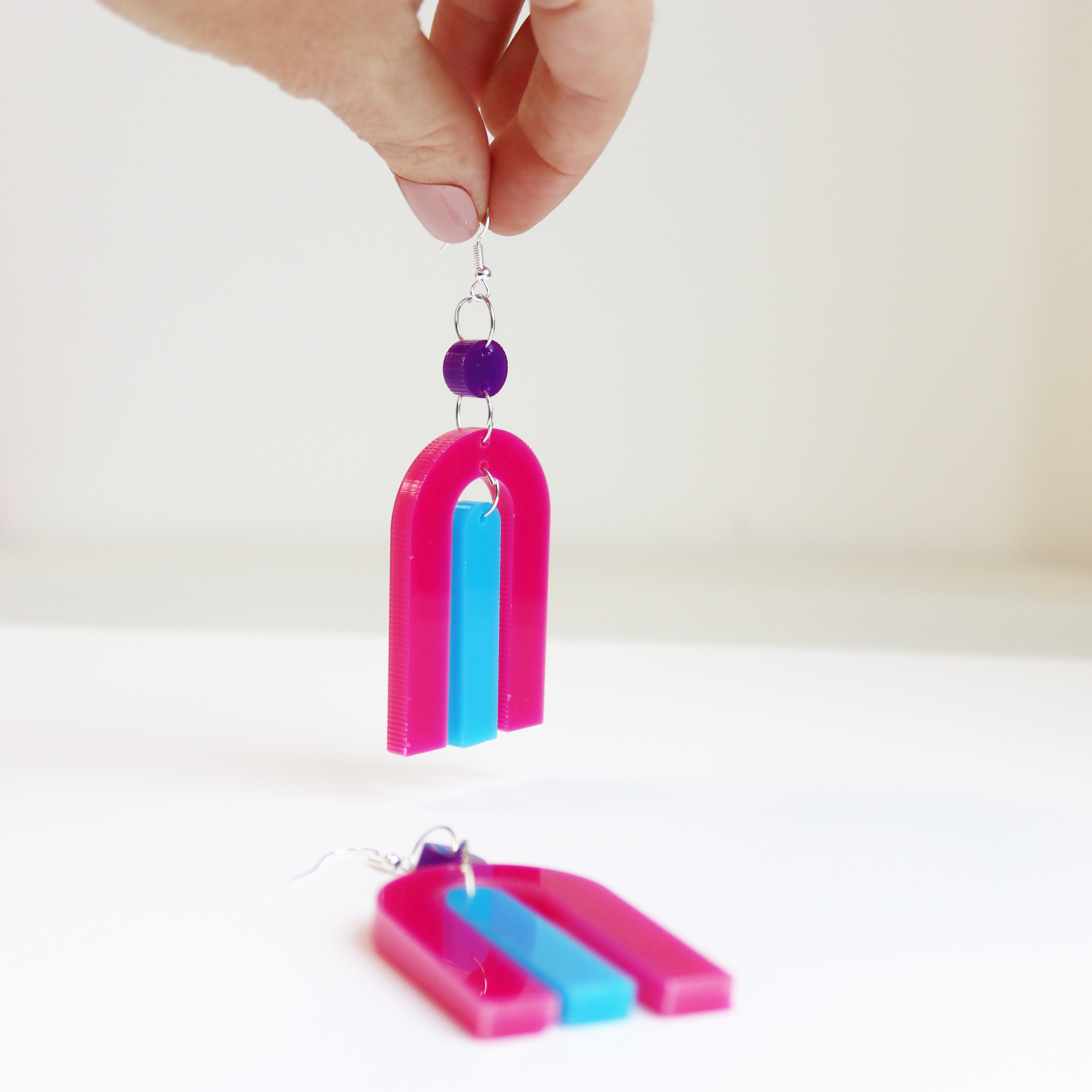 modern bright and colourful geometric arch dangle earrings cut from a purple, pink and turquoise acrylic shown on a mirrr background