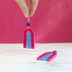 modern bright and colourful geometric arch dangle earrings cut from a purple, pink and turquoise acrylic shown hanging from a woman's fingers