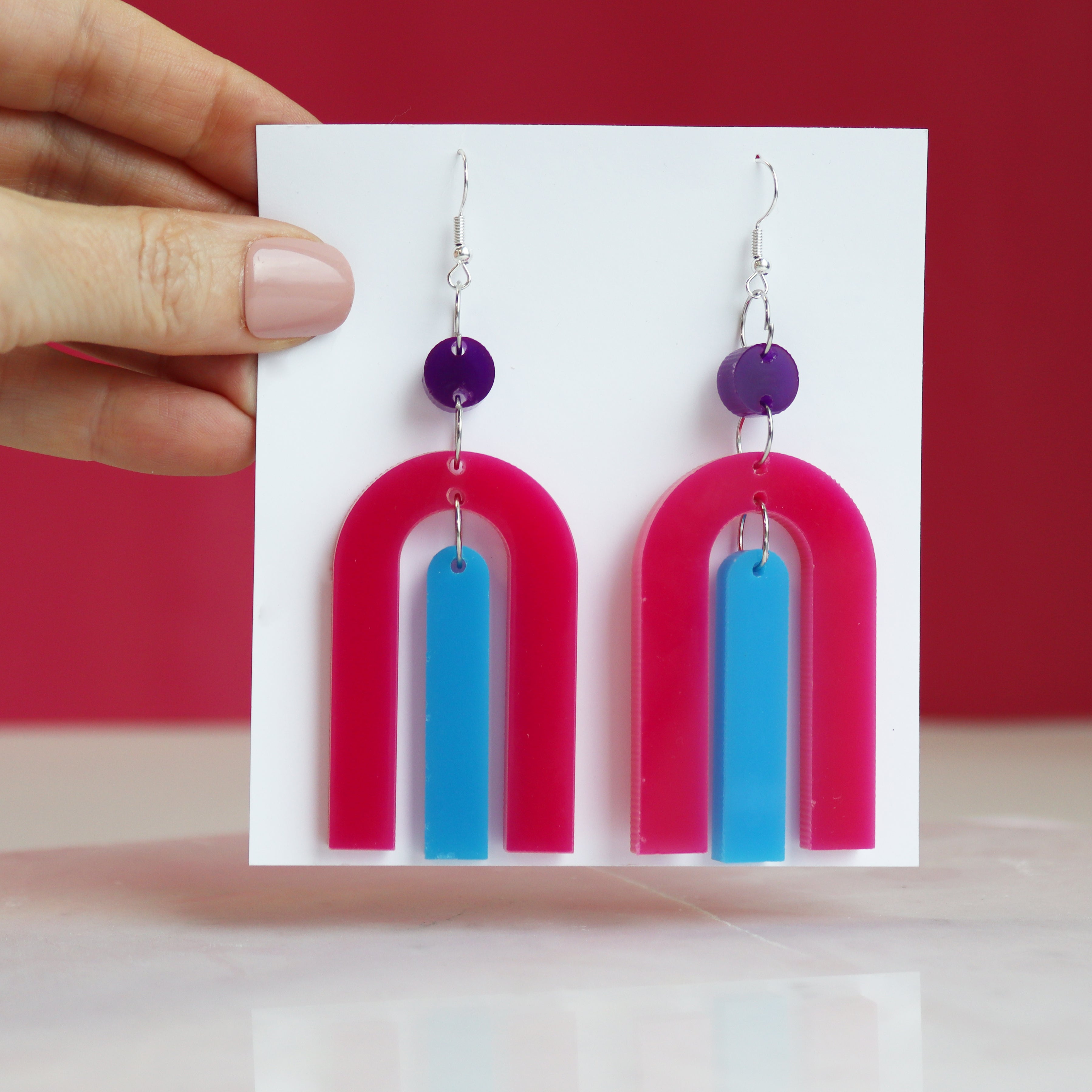 modern bright and colourful geometric arch dangle earrings cut from a purple, pink and turquoise acrylic shown hanging on backing card image 2