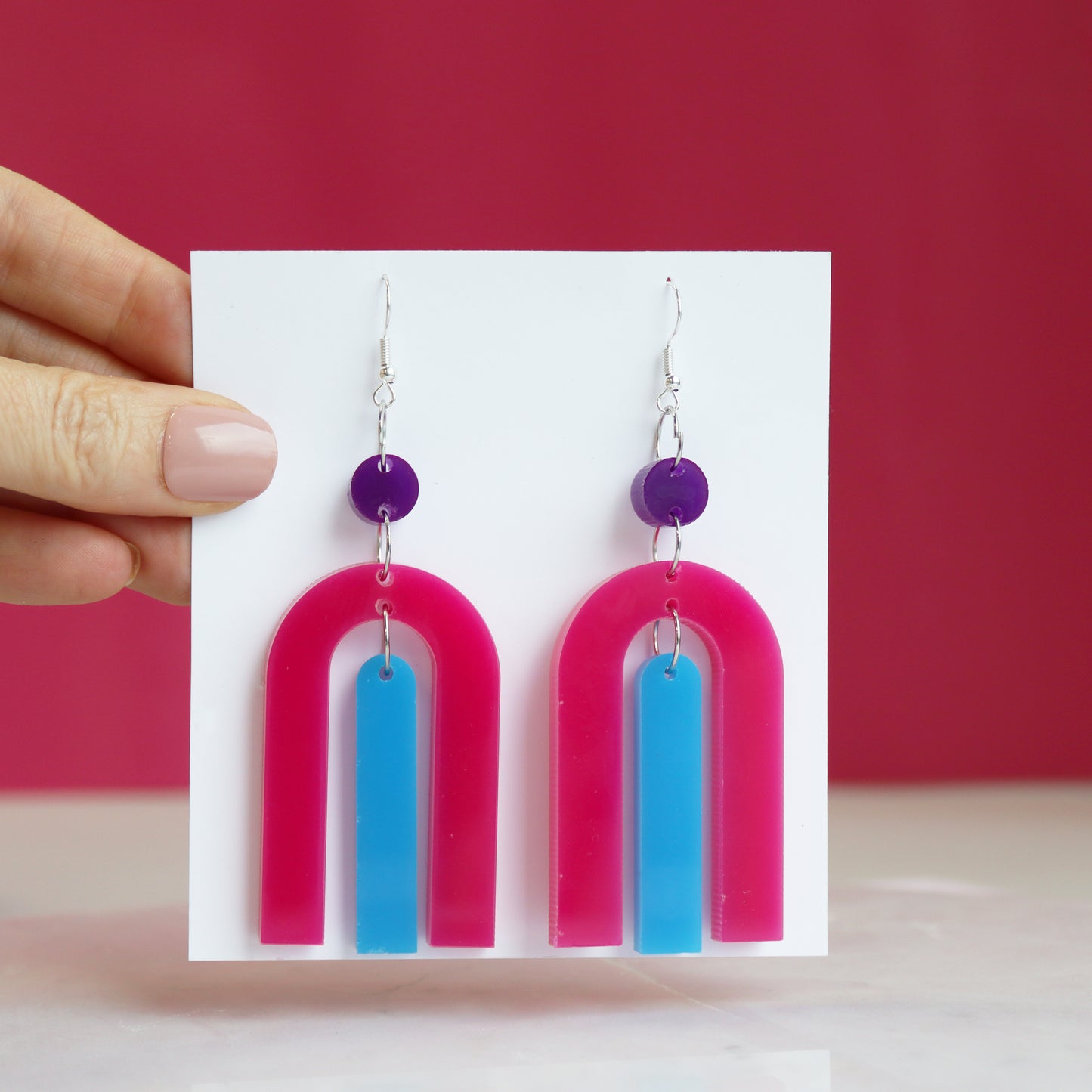 modern bright and colourful geometric arch dangle earrings cut from a purple, pink and turquoise acrylic shown hanging on backing card image 3
