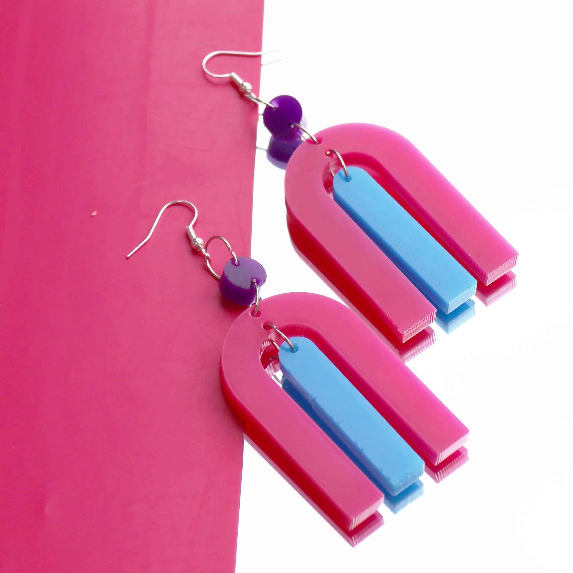 modern bright and colourful geometric arch dangle earrings cut from a purple, pink and turquoise acrylic shown on a mirrr background