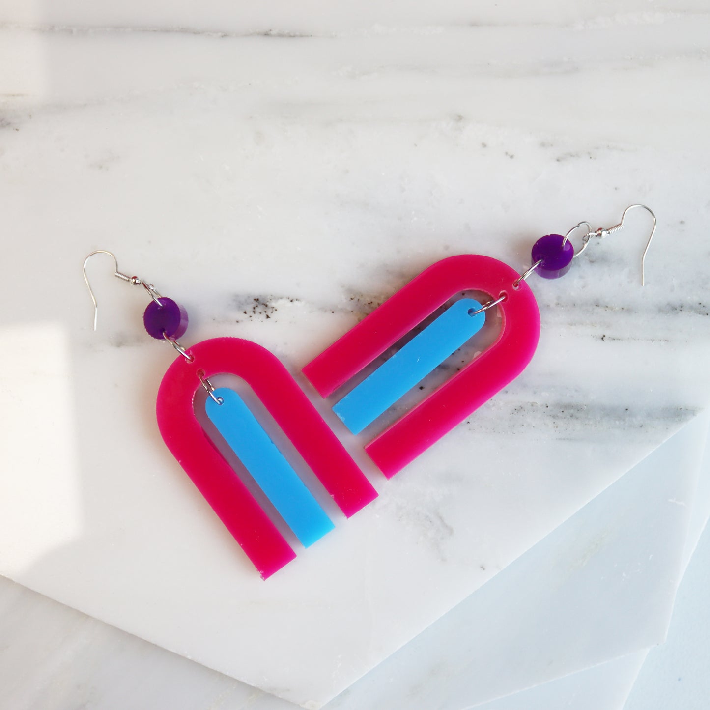 modern bright and colourful geometric arch dangle earrings cut from a purple, pink and turquoise acrylic shown on marble background