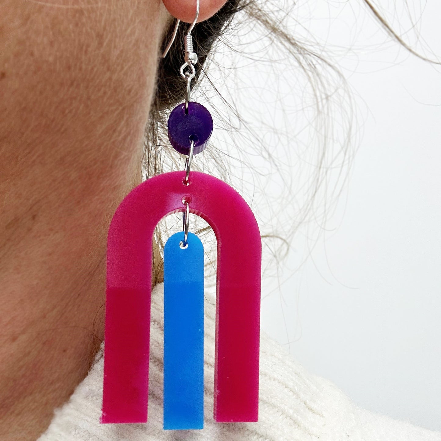 modern bright and colourful geometric arch dangle earrings cut from a purple, pink and turquoise acrylic shown on marble background
