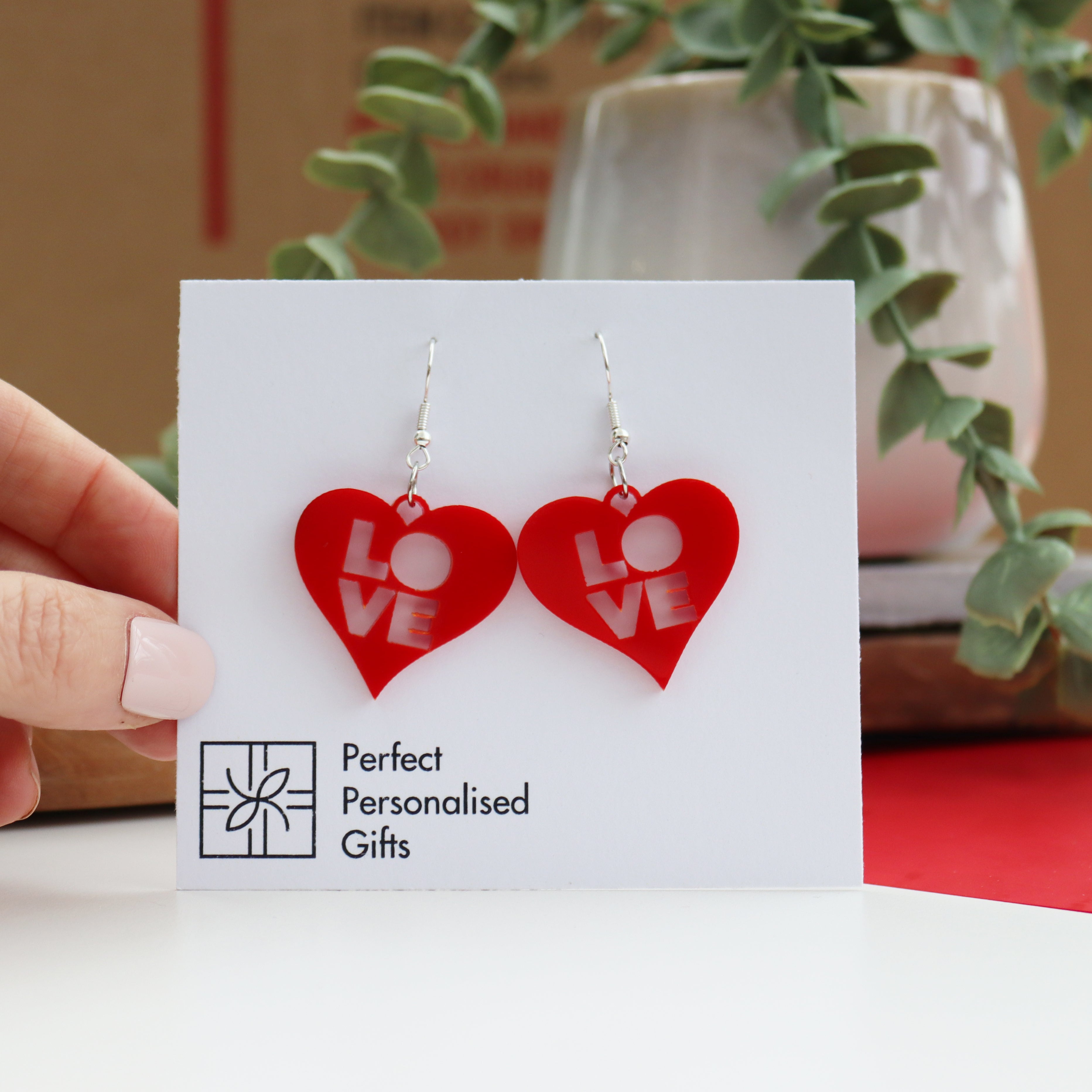 modern laser cut acrylic red valentines earrings with the word LOVE cut out from the centre of the heart shape on a plated silver hook