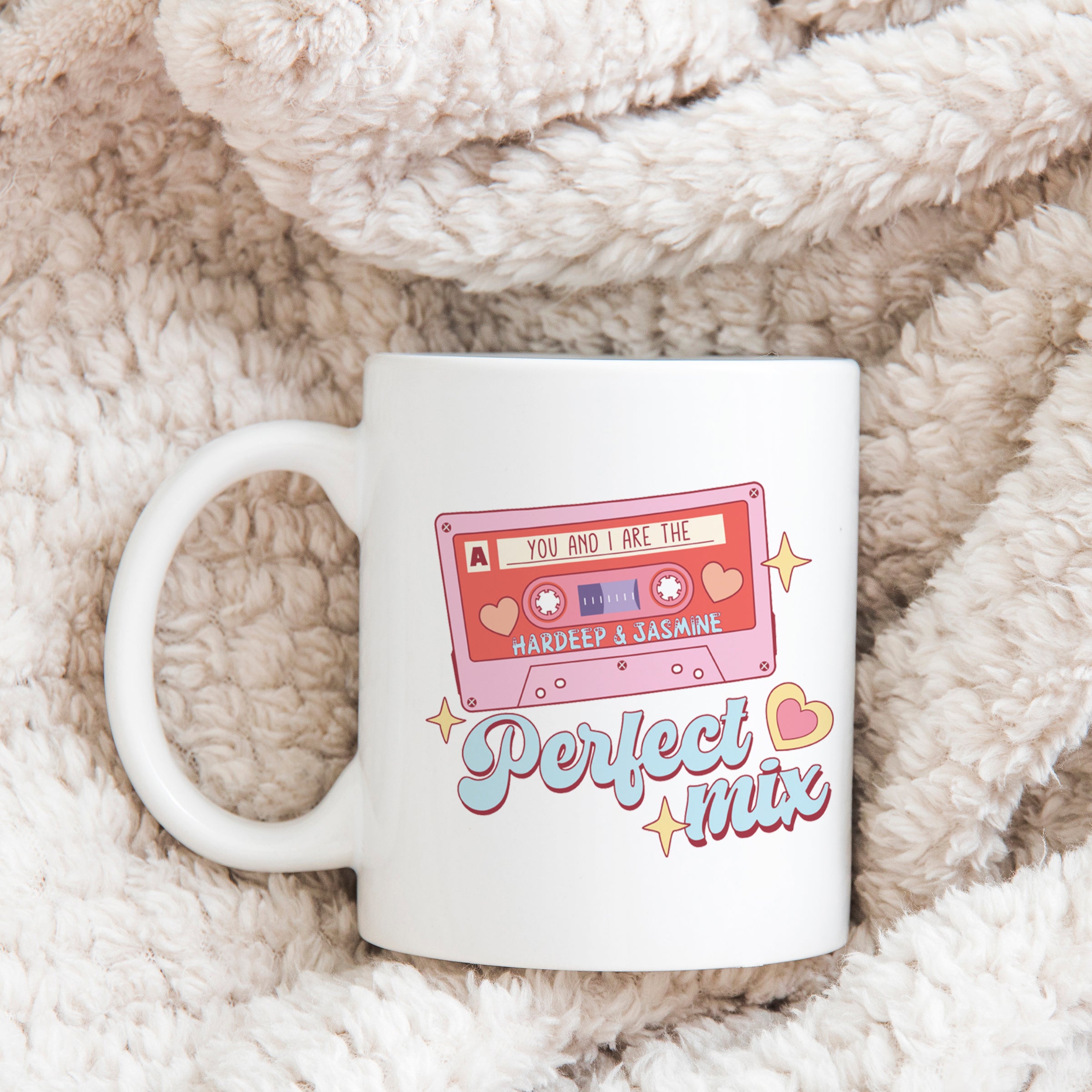 A white ceramic mug with a retro typographical print featuring the words 'We are a Perfect Mix' and a cassette tape graphic, placed on a cozy, textured surface.