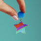 printed acrylic colourful handmade acrylic earrings with one earring being held on a turquoise background
