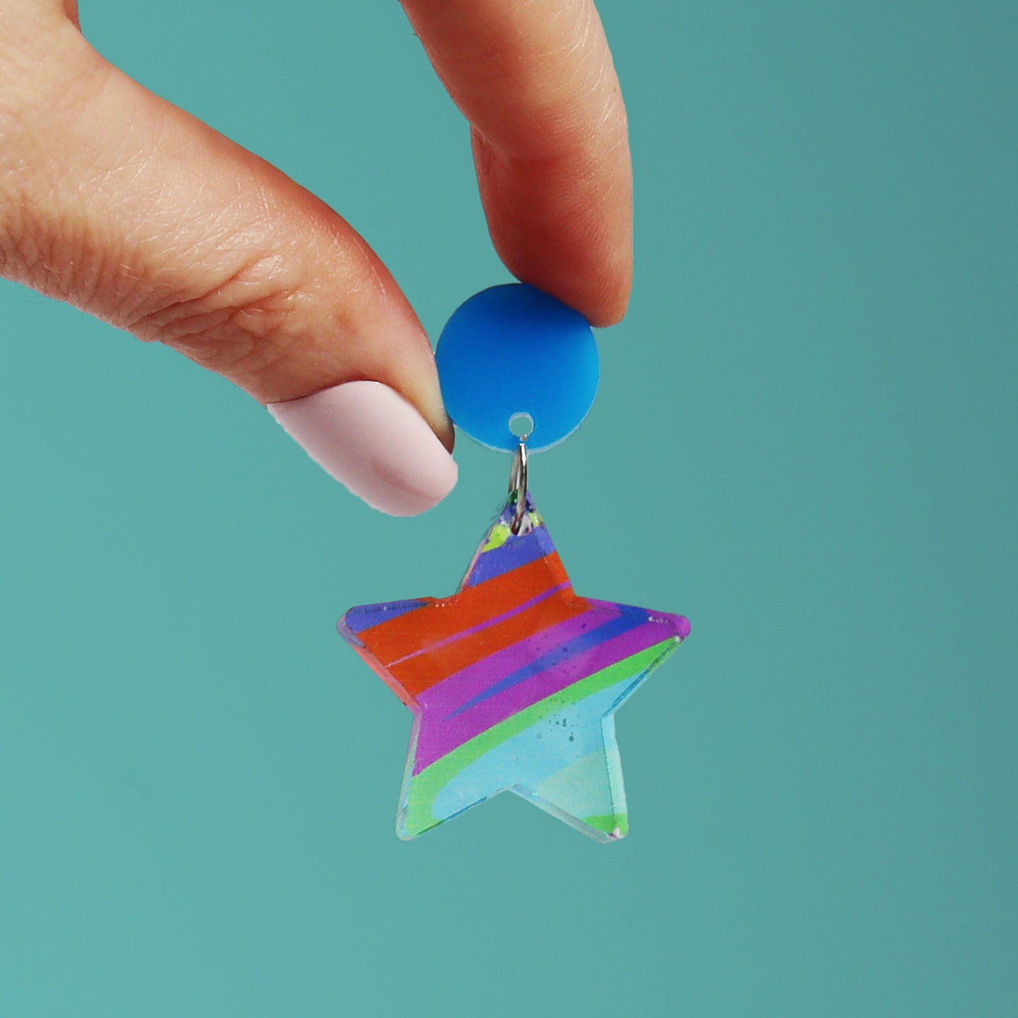 printed acrylic colourful handmade acrylic earrings with one earring being held on a turquoise background