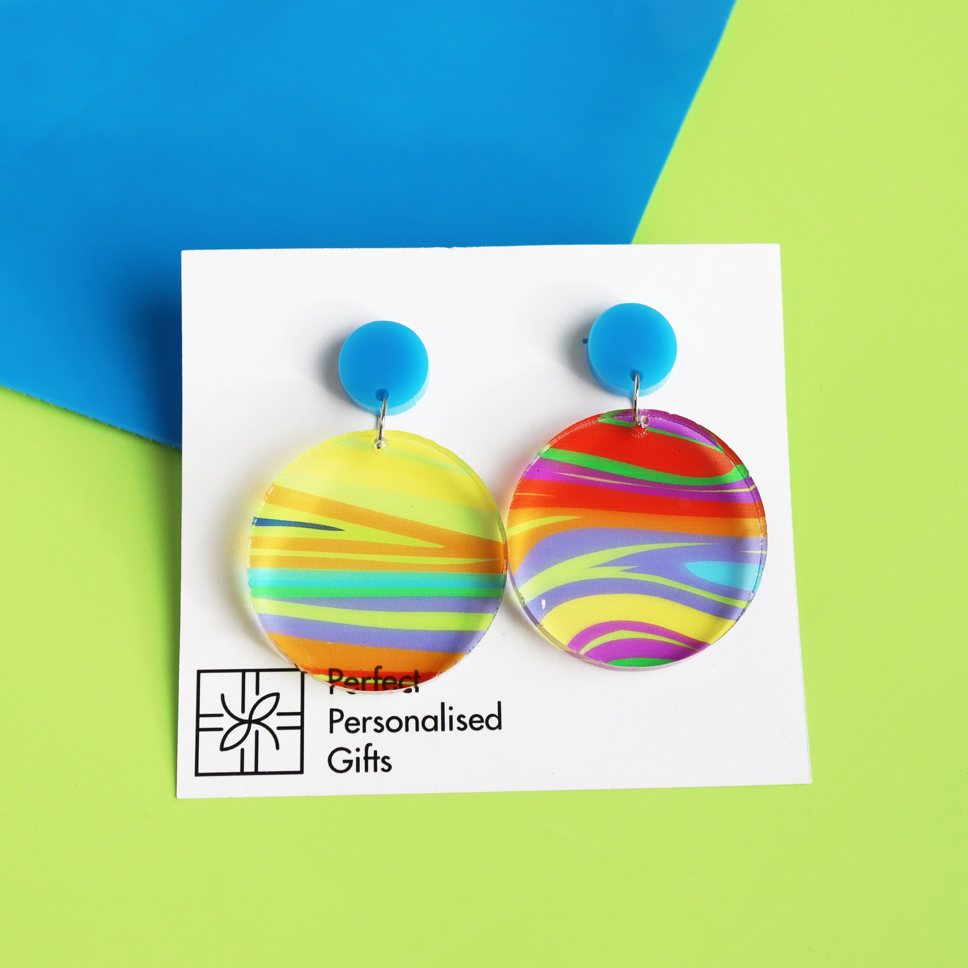 printed acrylic colourful mismatch earrings that have a round blue acrylic stud top and hanging printed acrylic circle hanging on a white card background on green neon