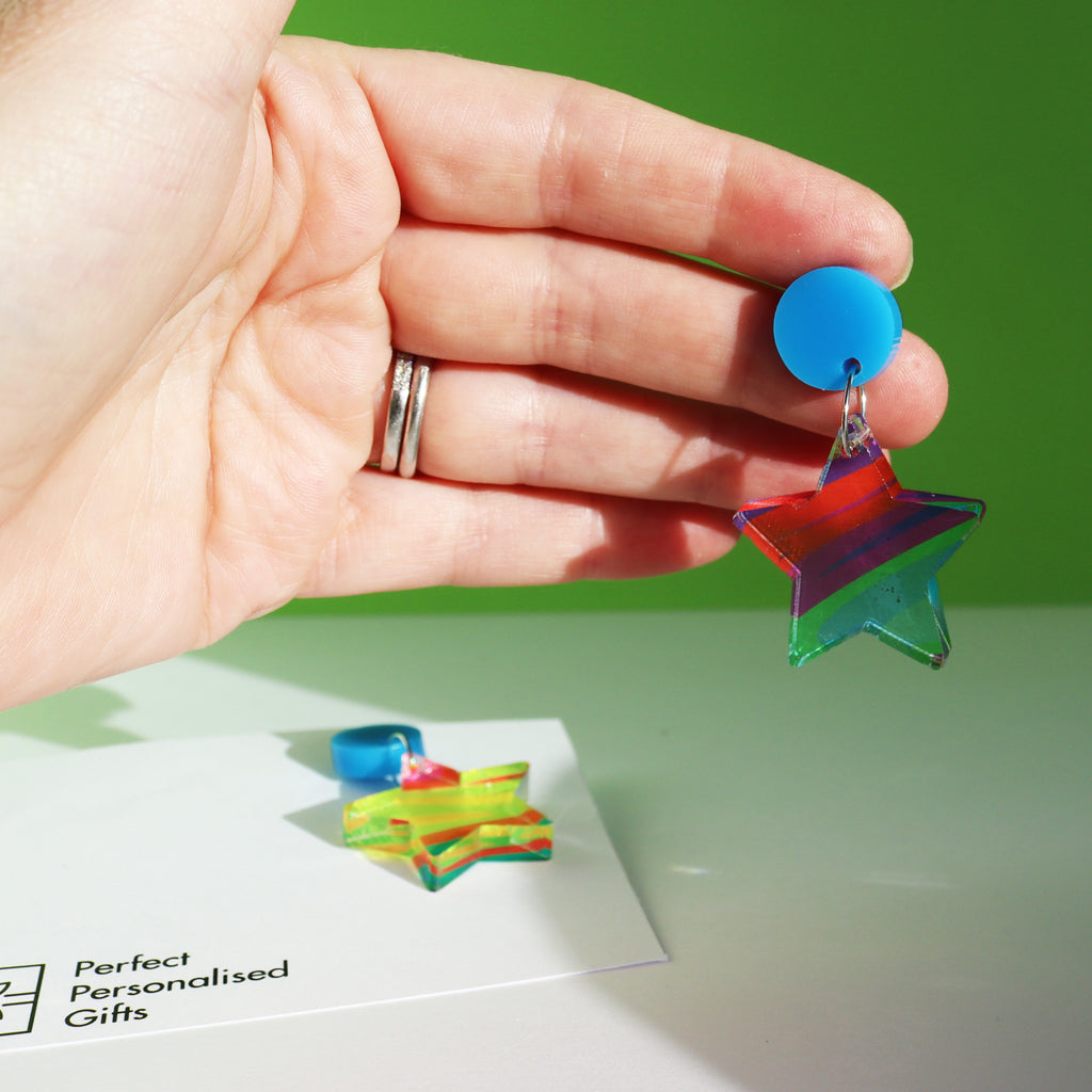 printed acrylic colourful mismatch earrings that have a round blue acrylic stud top and hanging printed acrylic star shown in a womans hand