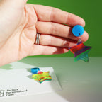 printed acrylic colourful mismatch earrings that have a round blue acrylic stud top and hanging printed acrylic star shown in a womans hand