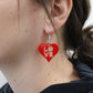 red laser cut acrylic heart earrings close up shown hanging from an ear