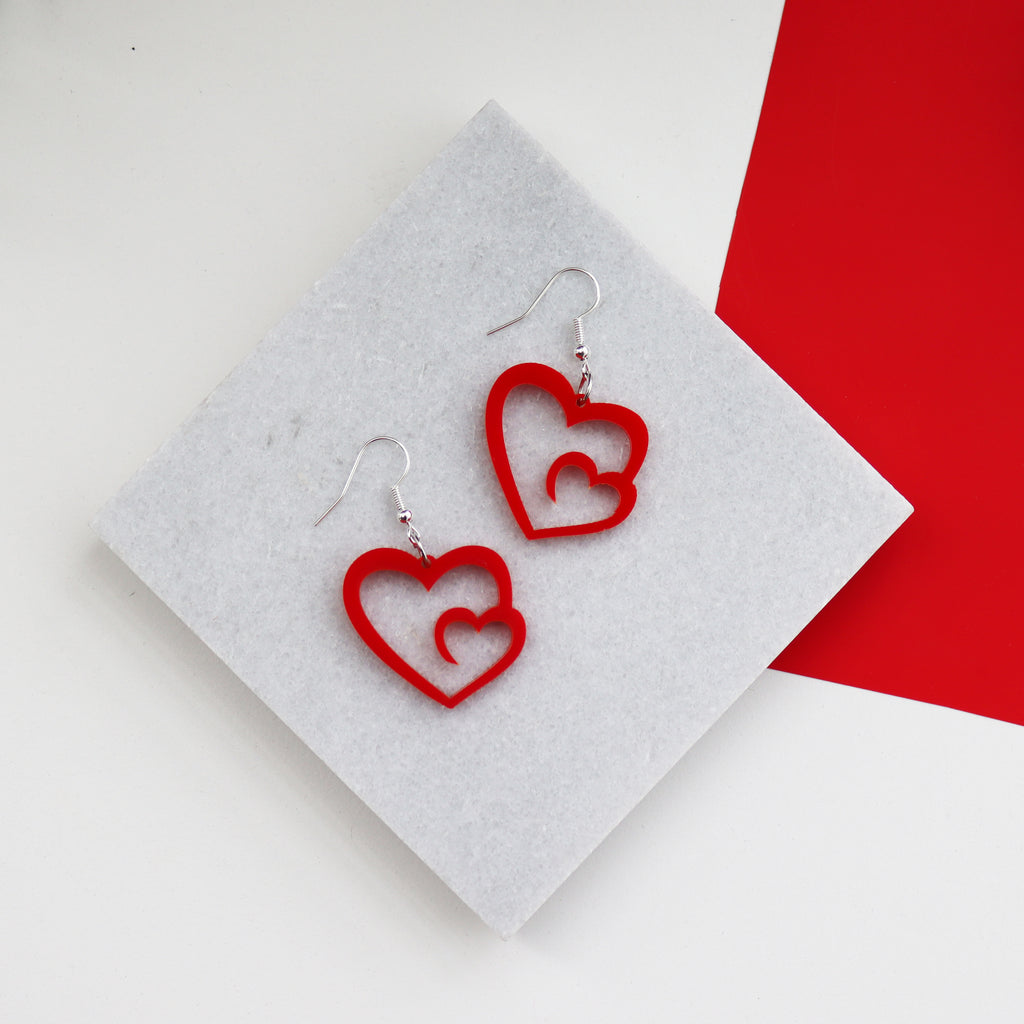 red laser cut acrylic heart earrings with love cut out from the centre shown on a marble background