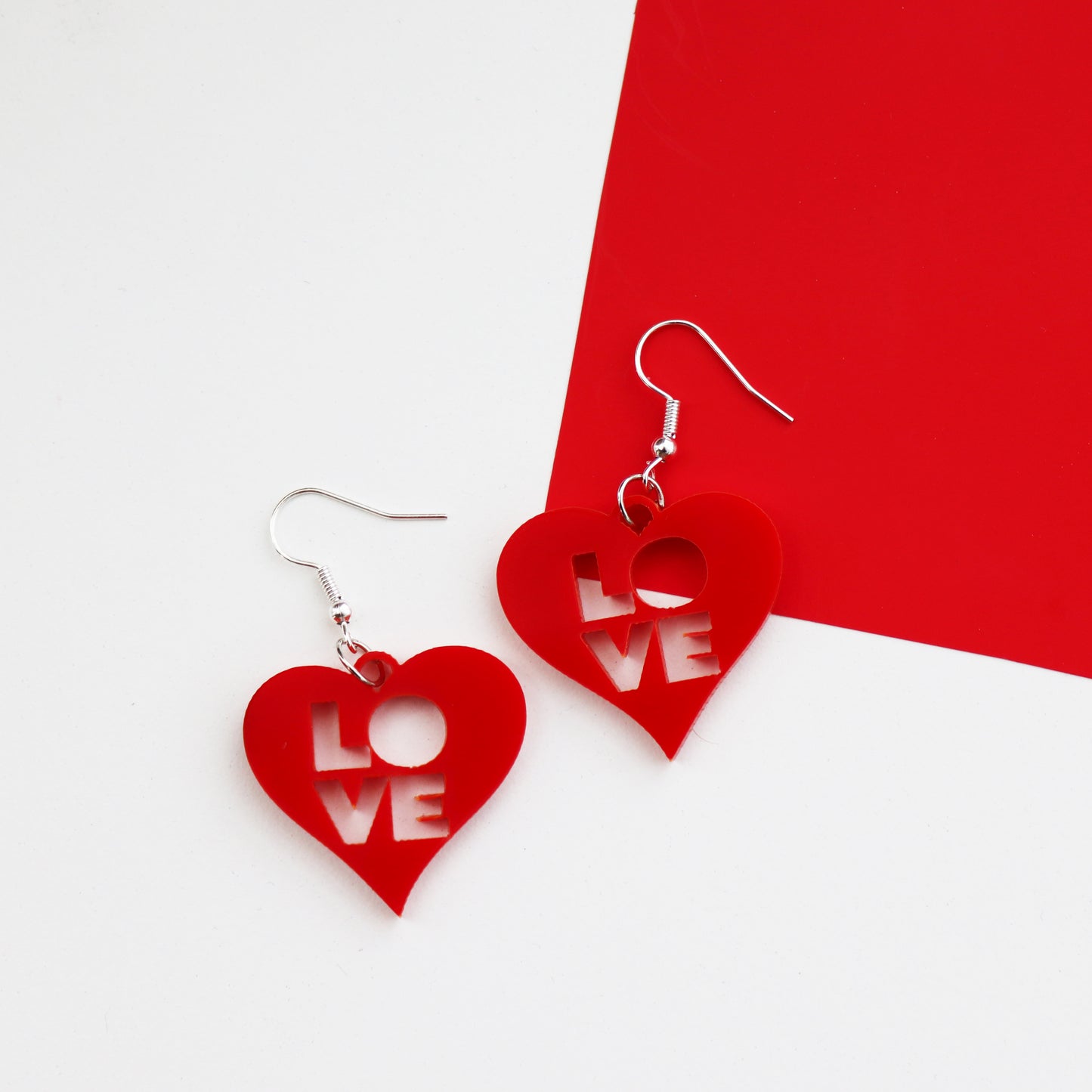 red laser cut acrylic heart earrings with love cut out from the centre shown on a red and white background